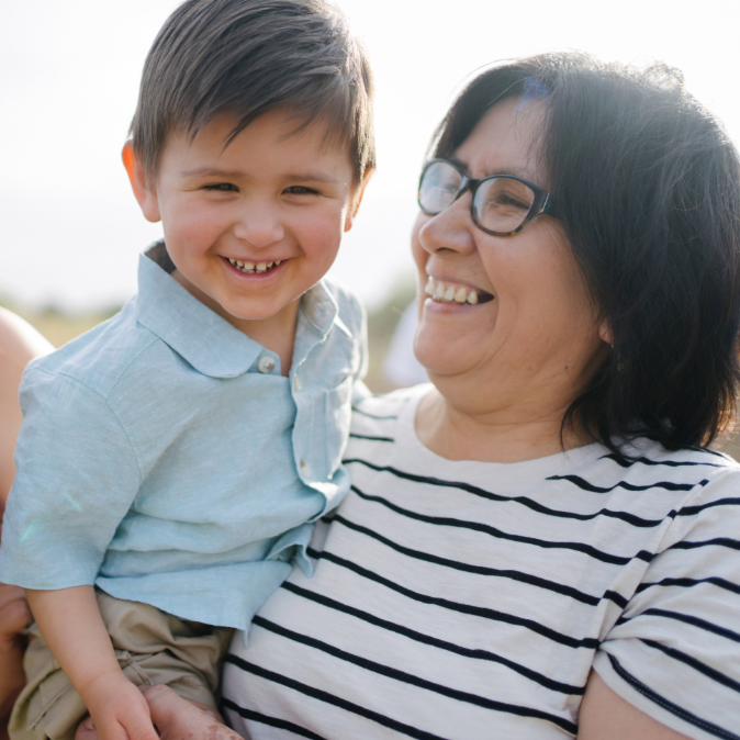 Latina grandmother smiling and holding smiling young grandson